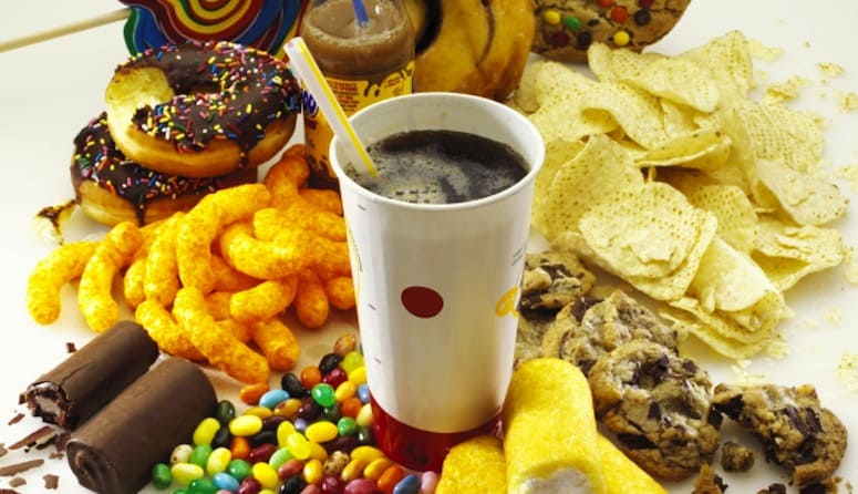Aliments riches en calories et en sucres variés Assortiment de snacks sucrés et salés avec soda sur une surface blanche.